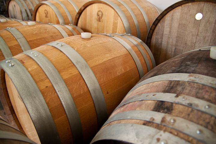 Rząd dębowych beczek z metalowymi obręczami, niektóre z logo, w magazynie lub piwnicy.