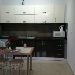 Nowoczesna kuchnia z białymi górnymi szafkami i ciemnymi dolnymi, stół z krzesłami i rośliną, butelka na szafkach.