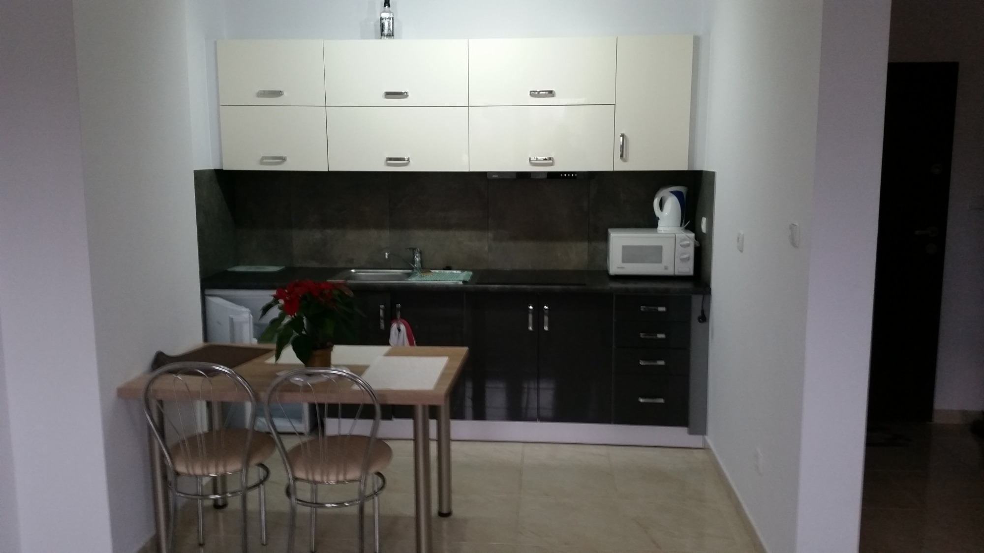 Nowoczesna kuchnia z białymi górnymi szafkami i ciemnymi dolnymi, stół z krzesłami i rośliną, butelka na szafkach.