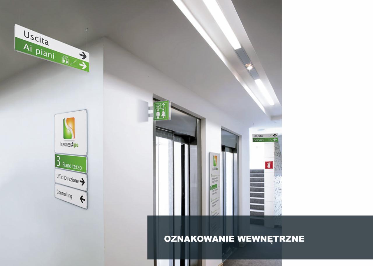 Wnętrze biurowca z systemem oznakowania: podwieszane tablice kierunkowe, tabliczki informacyjne na ścianie, wskazujące kierunki do biur i toalet.