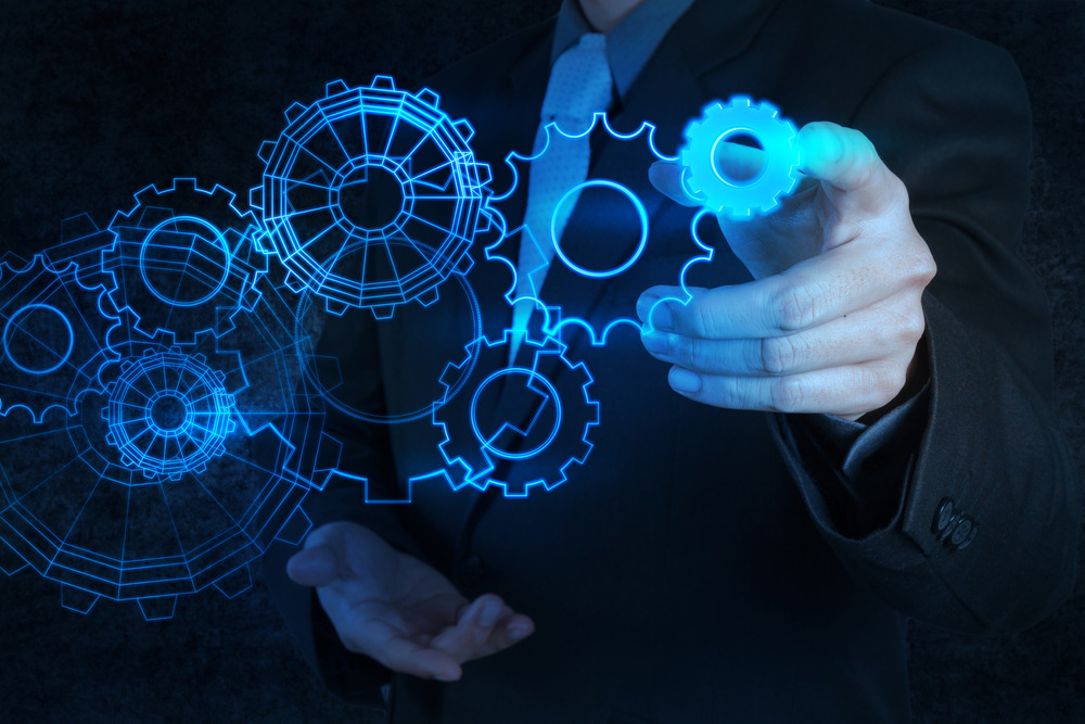 Mężczyzna w garniturze manipuluje cyfrowymi, neonowymi kołami zębatymi na ciemnym tle.