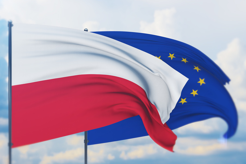 Flaga Polski i Unii Europejskiej powiewająca na wietrze na tle błękitnego nieba z delikatnymi chmurami.