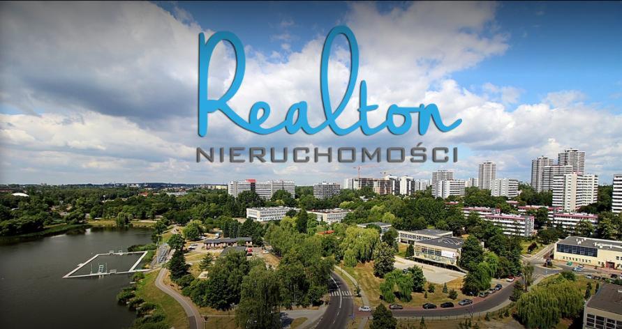 Panorama miasta z widokiem na jezioro, budynki mieszkalne i biurowce, z logo firmy 'Realton Nieruchomości' na pierwszym planie.