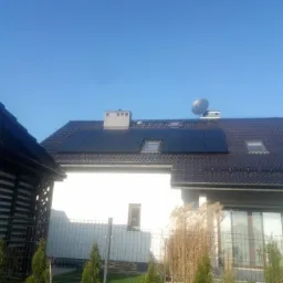 Dom jednorodzinny z zainstalowanymi panelami fotowoltaicznymi na dachu, widoczne okna dachowe i antena satelitarna.
