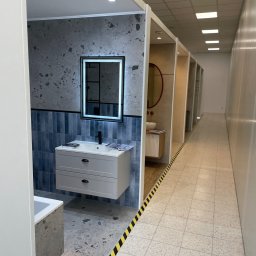 Supra Mateusz Kuśnierz - Nowoczesna aranżacja łazienki z umywalką i lustrem LED w Mielcu. Wykończenie w odcieniach szarości i błękitu, płytki imitujące beton. Ekspozycja w salonie.