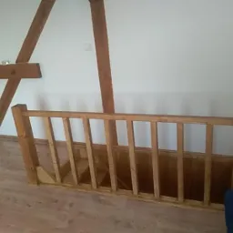 Drewniana balustrada schodów na poddaszu z widocznymi belkami stropowymi w odnowionym wnętrzu.