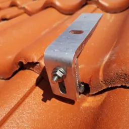 Metalowy uchwyt z nakrętką przymocowany do pomarańczowej dachówki ceramicznej, element systemu montażowego.