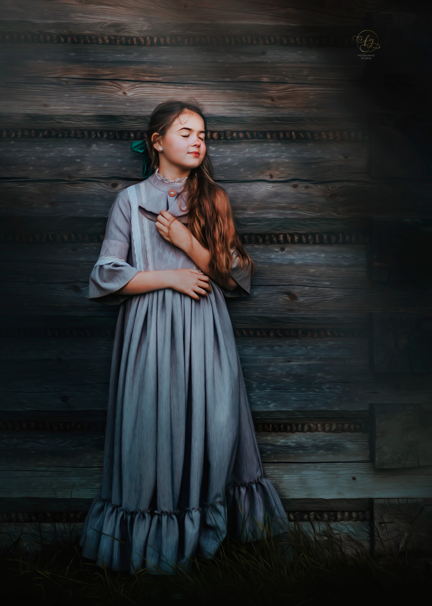 Młoda dziewczyna w szarej sukience z zieloną wstążką we włosach, pozuje na tle starej drewnianej ściany z zamkniętymi oczami.