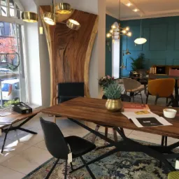 Jadalnia z dużym drewnianym stołem na czarnych nogach, czarne krzesła, dywan w orientalne wzory, w tle dekoracyjna ściana z litego drewna i widok z okna.