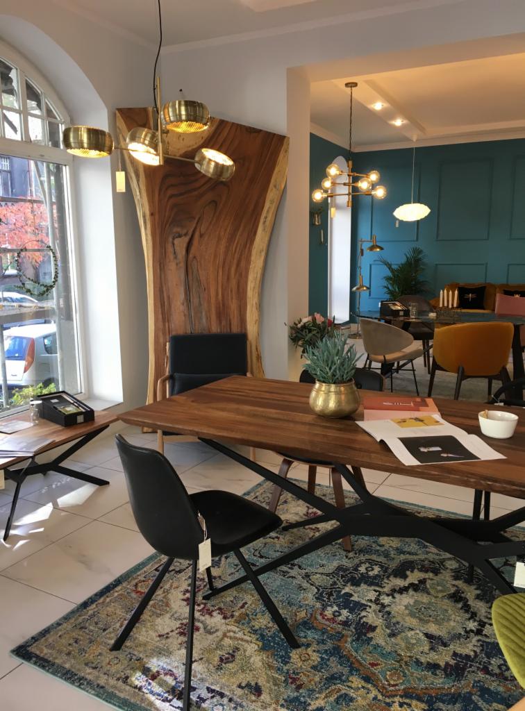 Jadalnia z dużym drewnianym stołem na czarnych nogach, czarne krzesła, dywan w orientalne wzory, w tle dekoracyjna ściana z litego drewna i widok z okna.