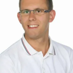 Portret uśmiechniętego mężczyzny w okularach i białej koszulce polo z granatowo-czerwonym paskiem na kołnierzyku, na białym tle.