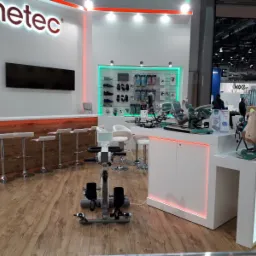 Ekspozycja sprzętu rehabilitacyjnego marki Kinetec na targach, z widocznym rowerem rehabilitacyjnym, urządzeniami do ćwiczeń kończyn górnych i dolnych oraz elementami wyposażenia stoiska, takimi...