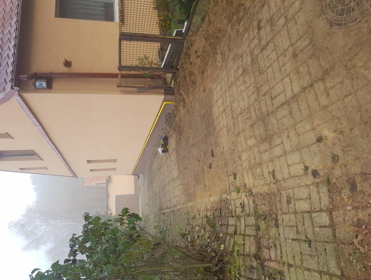 Elewacja budynku z żółtym przyłączem gazowym biegnącym wzdłuż ściany, widok z poziomu brukowanego chodnika.