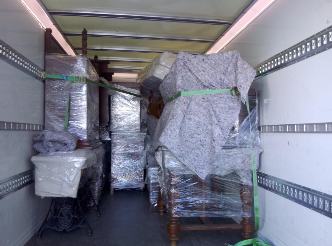 Wnętrze furgonetki załadowane meblami zabezpieczonymi folią stretch, kocami i pasami transportowymi, gotowymi do przewozu.