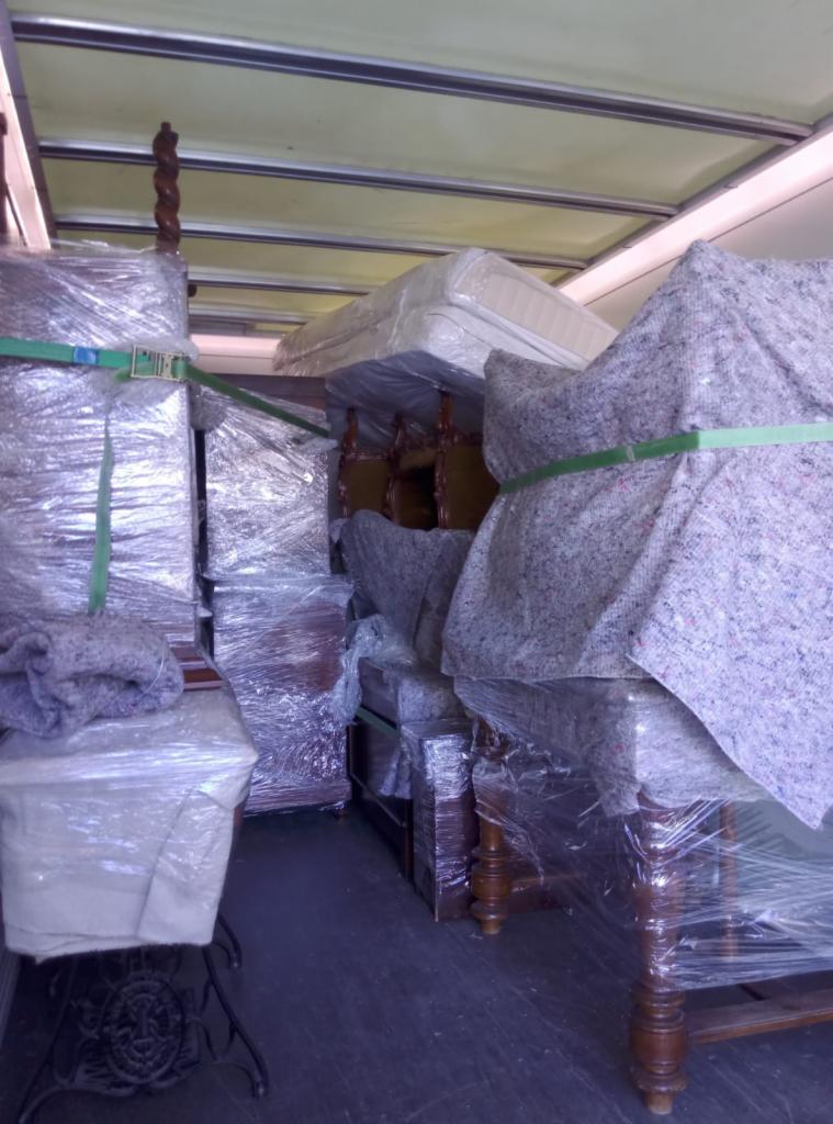 Wnętrze furgonetki załadowane meblami zabezpieczonymi folią stretch, kocami transportowymi i pasami mocującymi, gotowymi do transportu.