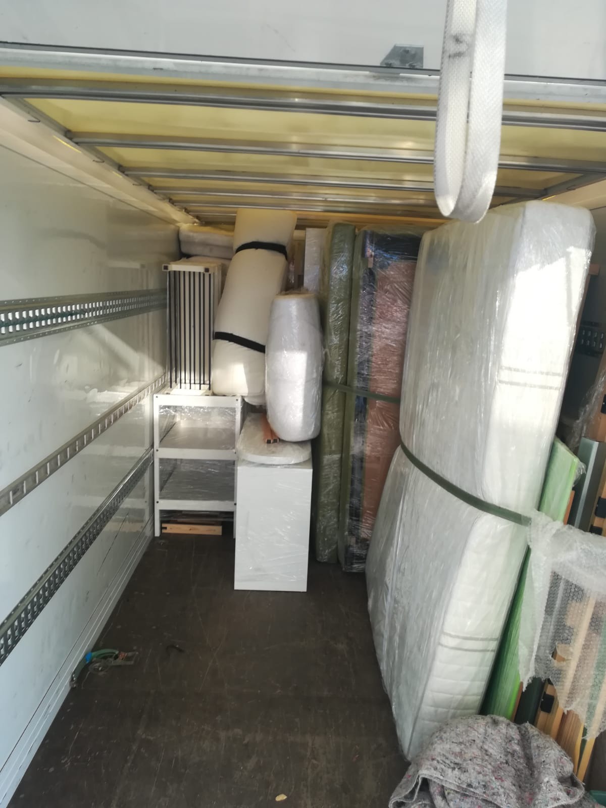 Wnętrze furgonetki załadowane meblami i sprzętami, zabezpieczonymi folią stretch i pasami transportowymi, gotowymi do przewozu.