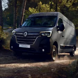 Nowoczesny, grafitowy bus Renault Master na leśnej, szutrowej drodze, z widocznym logo i nazwą modelu na przedniej masce.