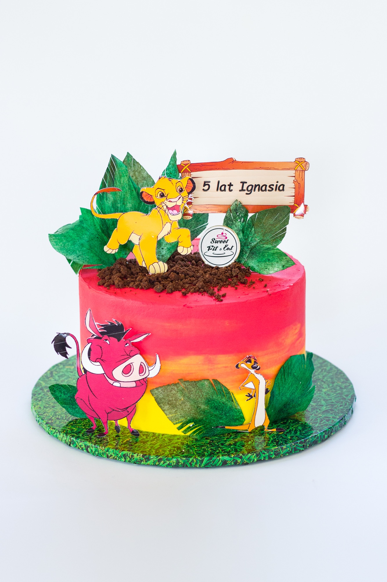 Tort urodzinowy w stylu Króla Lwa z figurkami Simby, Timona i Pumby oraz napisem '5 lat Ignasia' na drewnianym szyldzie.