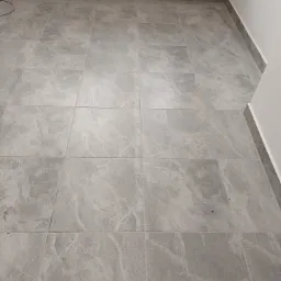 Nowo ułożona, szara, marmurkowa podłoga z płytek w jasnym pomieszczeniu, widoczne listwy przypodłogowe i gniazdka elektryczne w ścianie.