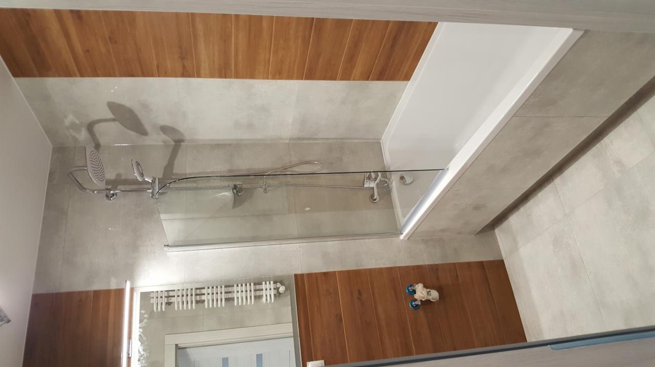 Nowoczesna łazienka z kabiną prysznicową ze szklanym panelem, drewnopodobnymi i szarymi płytkami oraz chromowaną armaturą.