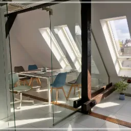 Jasna sala konferencyjna na poddaszu z ukośnymi oknami dachowymi, szklaną ścianą i drewnianą konstrukcją nośną, wyposażona w stół i krzesła.