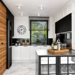 Nowoczesna kuchnia w bieli i czerni z drewnianą zabudową, marmurową podłogą i wyspą z przeszklonymi szafkami, na blacie butelki wina i kieliszki.