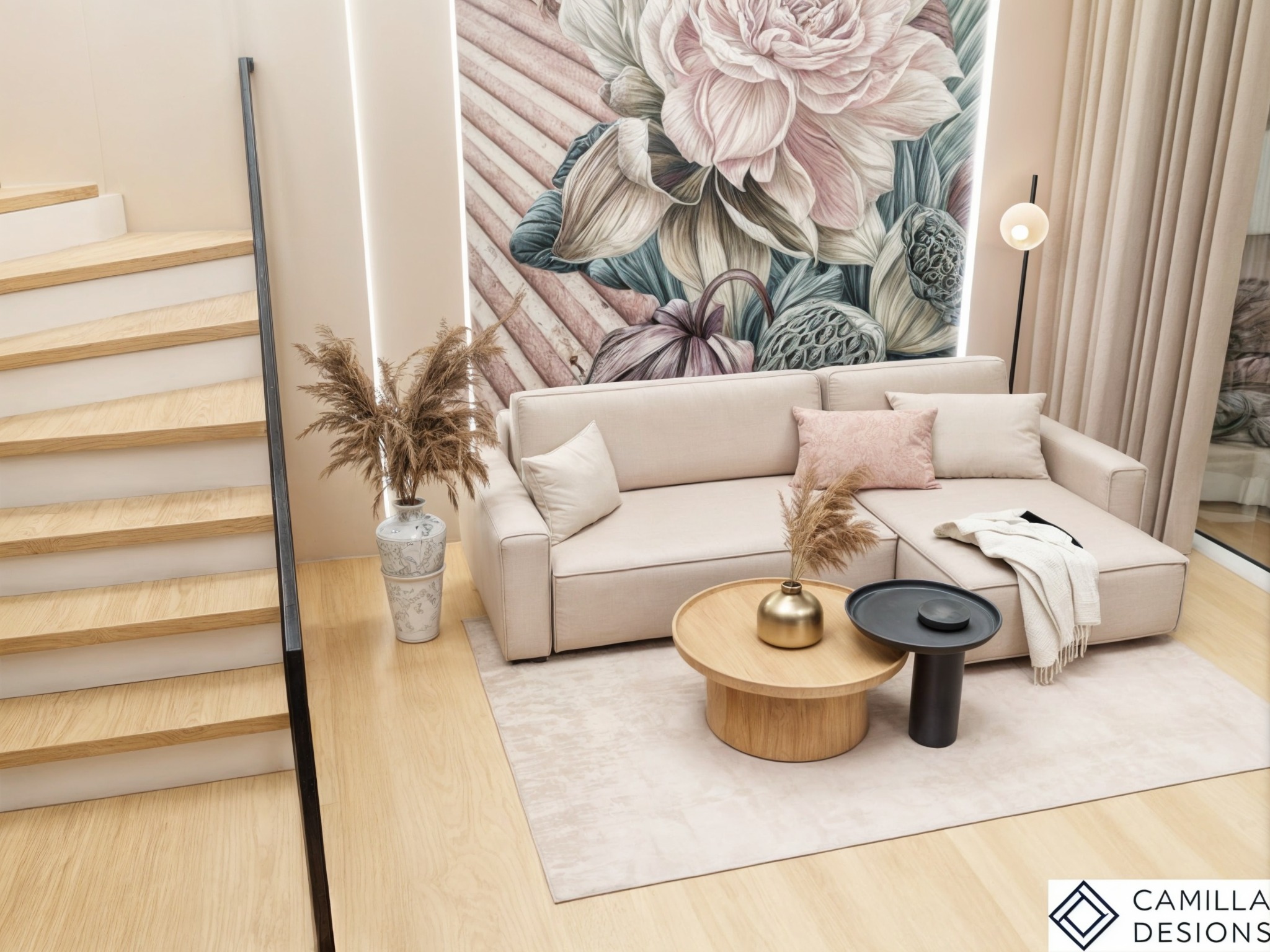 Jasny salon z drewnianymi schodami, beżową sofą narożną, okrągłym drewnianym stolikiem kawowym i tapetą w kwiaty, oświetlony lampą podłogową.