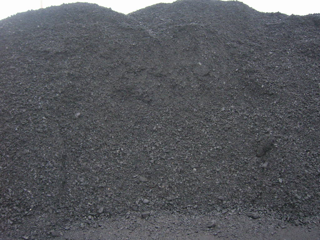 Góra czarnego, drobnego miału węglowego, oświetlona naturalnym światłem dziennym, z widoczną strukturą i małymi kamieniami.