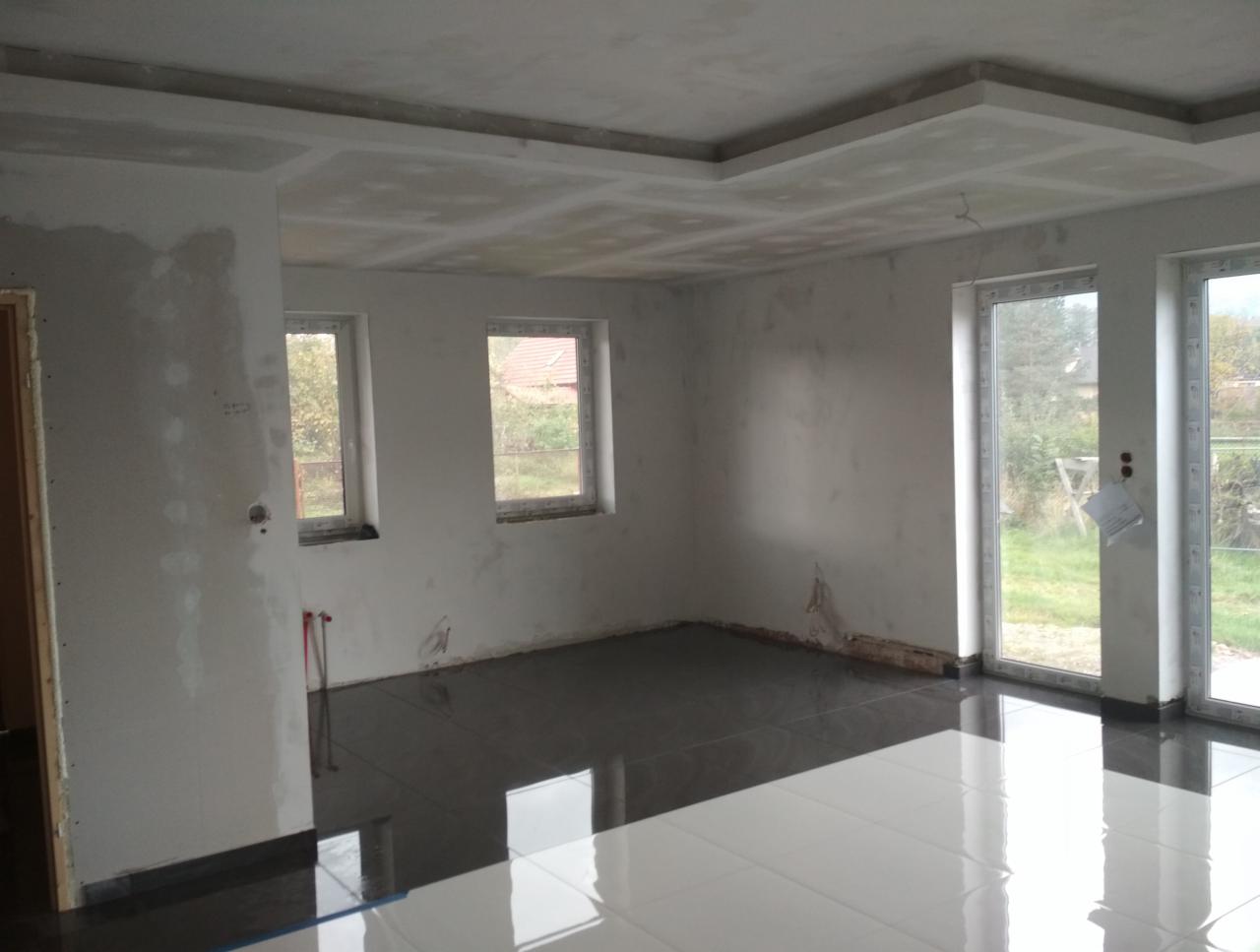 Pokój w trakcie prac wykończeniowych: położona ciemna glazura podłogowa, ściany po szpachlowaniu, przygotowane do malowania, widoczny sufit podwieszany z płyt gipsowo-kartonowych.