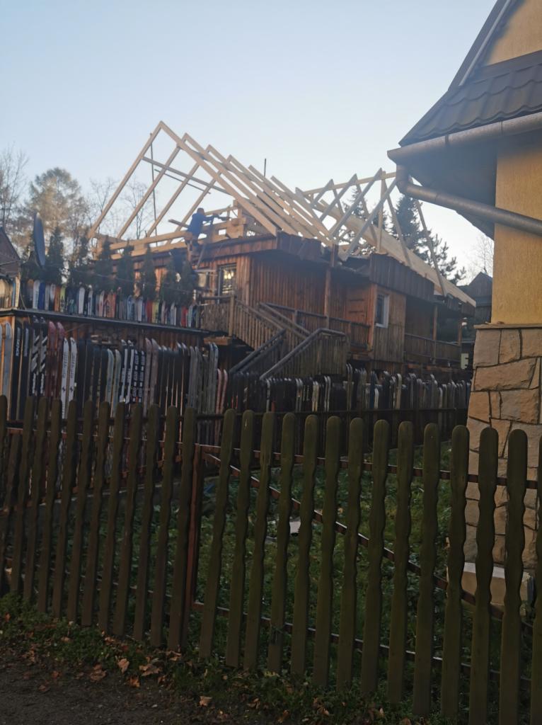 Konstrukcja nowego dachu na drewnianym domu w Zubrzycy Górnej. Widoczny cieśla na drabinie i drewniane elementy więźby dachowej.