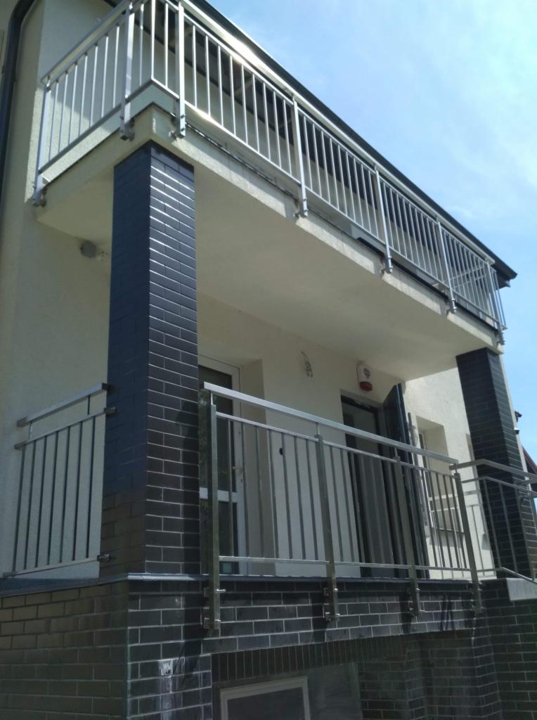 Dwu-poziomowy balkon z nierdzewnymi, spawane balustradami i czarnymi, ceglanymi filarami, widok z dołu.