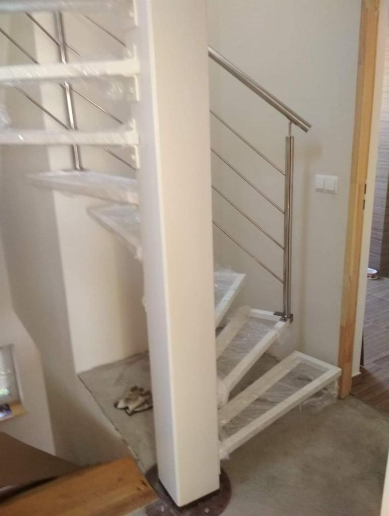 Wewnętrzne schody spiralne z metalową balustradą, zabezpieczone folią ochronną podczas montażu.