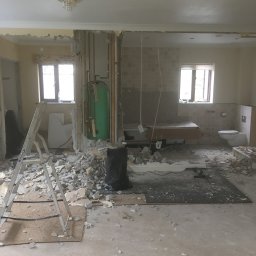 Herba-Tech - Rozbiórka łazienki z widocznymi instalacjami, gruzem i drabiną, przygotowanie do remontu z wiszącym kryształowym żyrandolem.