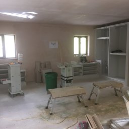 Herba-Tech - Wnętrze w trakcie montażu szafy wnękowej: widoczne narzędzia, drabiny, szafa z częściowo zamontowanymi półkami, okno z widocznymi narzędziami na parapecie, ślady po remoncie na podłodze.