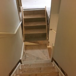 Herba-Tech - Widok z góry na schody w trakcie remontu, z widocznymi surowymi stopniami i przygotowanymi do malowania ścianami.