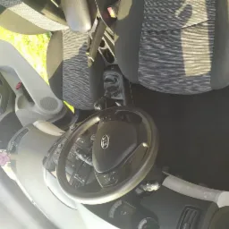 Wnętrze samochodu Kia z widocznym fotelem kierowcy, deską rozdzielczą, kierownicą z logo marki oraz odkurzaczem bezprzewodowym leżącym na dywaniku