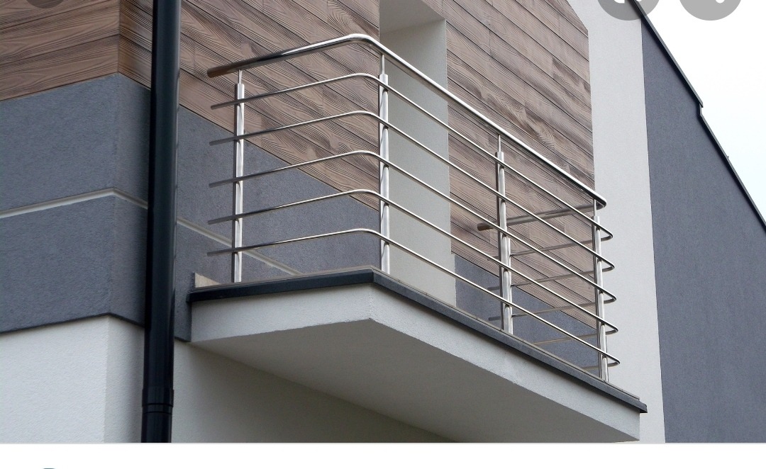 Nowoczesny balkon z prostą, stalową konstrukcją zabezpieczającą, na tle elewacji z elementami imitującymi drewno i szarego tynku.