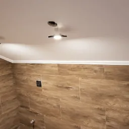 Ukończona łazienka w Nowej Wsi z drewnopodobnymi płytkami na ścianach, białym sufitem z zamontowanymi lampami punktowymi i dekoracyjną listwą przysufitową.