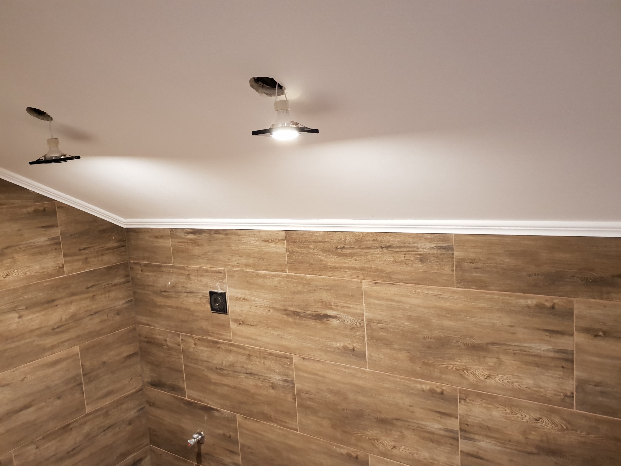 Ukończona łazienka w Nowej Wsi z drewnopodobnymi płytkami na ścianach, białym sufitem z zamontowanymi lampami punktowymi i dekoracyjną listwą przysufitową.