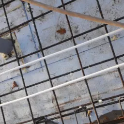 Zbrojenie fundamentów z rurami instalacyjnymi i szarą rurą kanalizacyjną, widok z góry. Elementy konstrukcyjne przygotowane do zalania betonem.