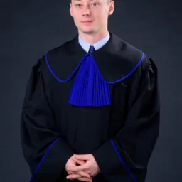Portret młodego mężczyzny w todze prawniczej z niebieskimi akcentami, ręce splecione na wysokości pasa, na ciemnoszarym tle.
