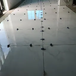 Układanie białych płytek podłogowych z marmurkowym wzorem, z systemem poziomowania płytek, w pomieszczeniu w Łobez.