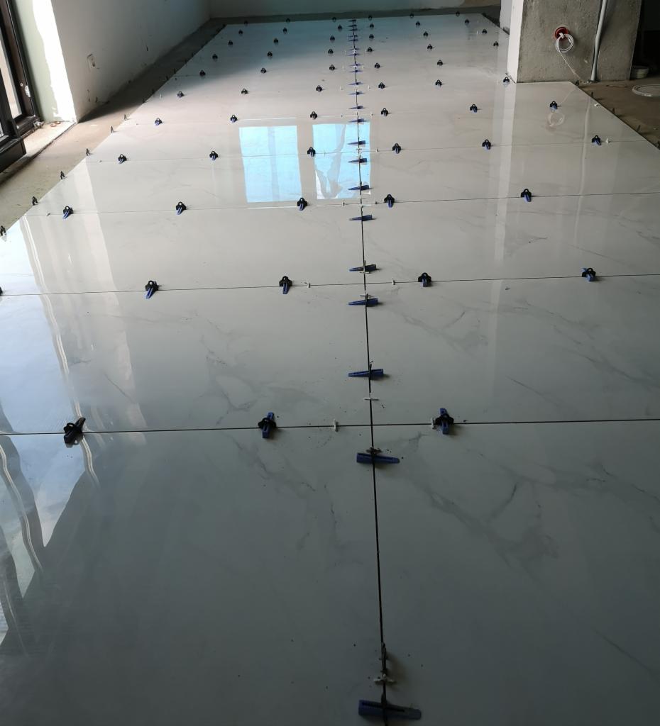 Układanie białych płytek podłogowych z marmurkowym wzorem, z systemem poziomowania płytek, w pomieszczeniu w Łobez.