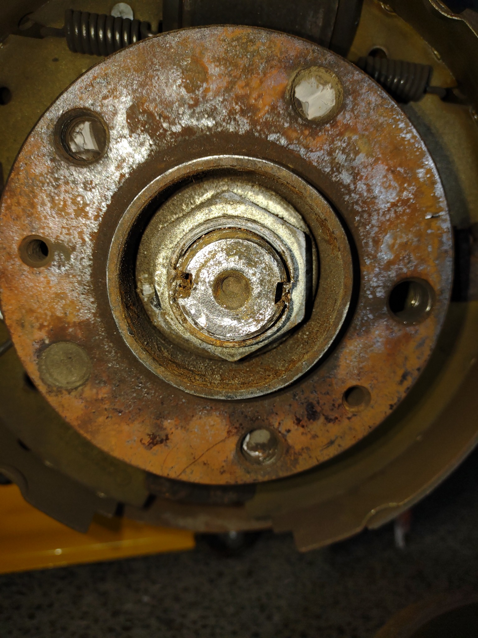 Zardzewiały element układu hamulcowego samochodu z centralną nakrętką zabezpieczoną zawleczką, widoczne ślady korozji i zużycia.