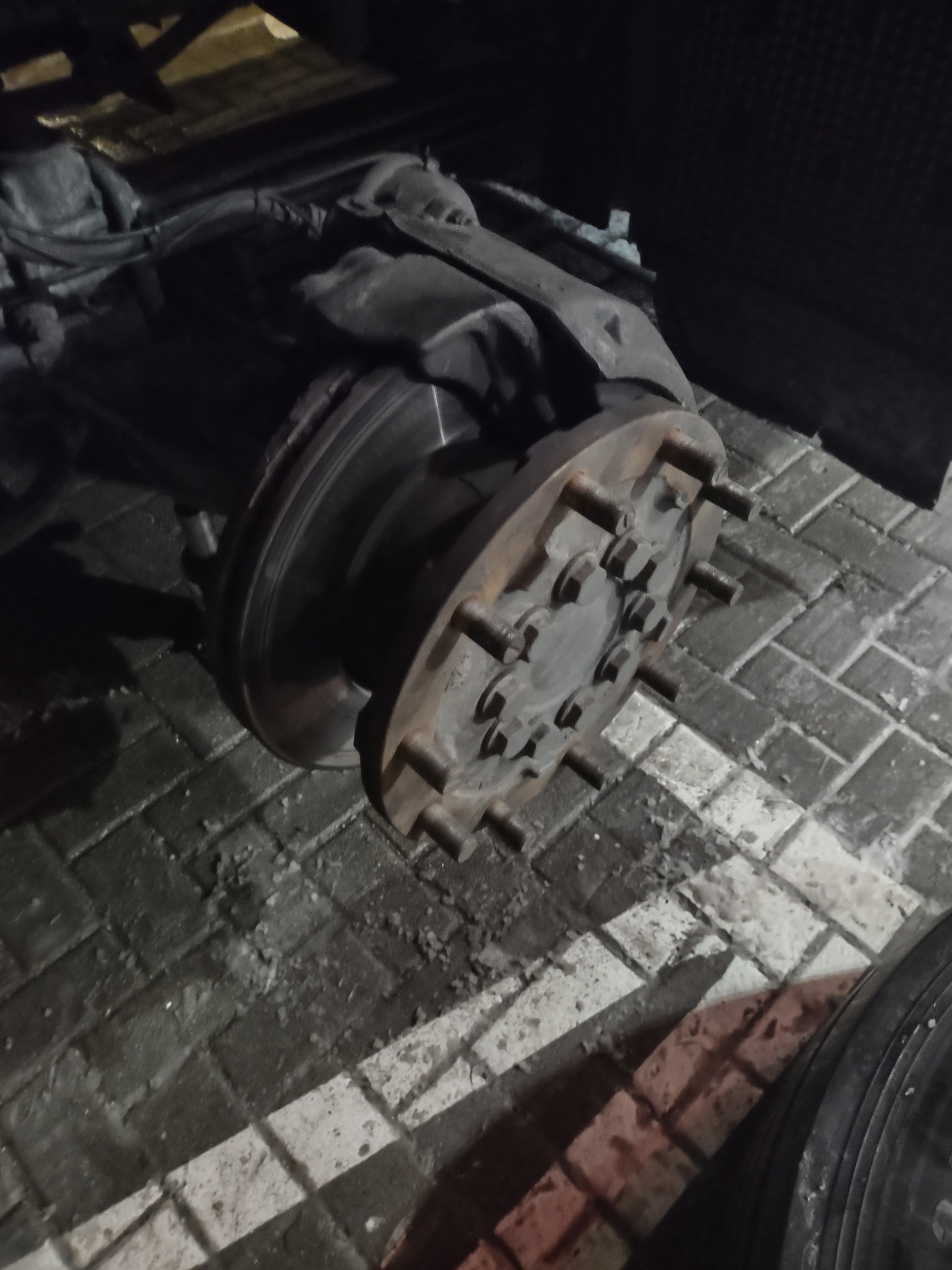 Zdjęcie z bliska przedstawia tarczę hamulcową i piastę koła ciężarówki na tle brukowanej nawierzchni, widoczne ślady eksploatacji i zabrudzenia.