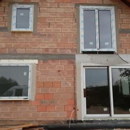 Oknosfera Tomasz Łapiński - Murowany budynek w trakcie montażu okien z białymi ramami, widoczne ślady zaprawy i wystające przewody.