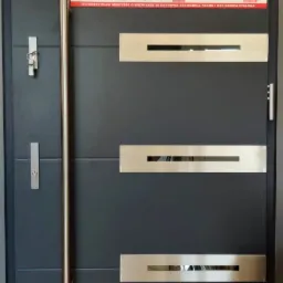 Nowoczesne, antracytowe drzwi zewnętrzne z długim, pionowym uchwytem ze stali nierdzewnej i poziomymi, prostokątnymi elementami dekoracyjnymi z otworem, prezentowane wraz z ulotką informacyjną...