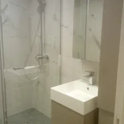 Wykończona łazienka z kabiną prysznicową z deszczownicą, umywalką nablatową na szafce w kolorze taupe oraz marmurowymi płytkami na ścianach.