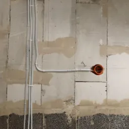 Ściana z betonu komórkowego z widocznymi przewodami elektrycznymi w peszlach i pomarańczowymi puszkami instalacyjnymi pod gniazdka.