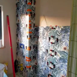 Montaż płytek z motywem roślinnym w rogu łazienki, z użyciem klipsów poziomujących i krzyżyków dystansowych, widoczna poziomica w pionie.